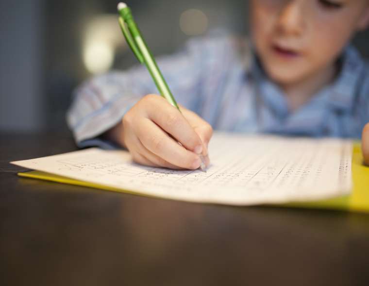 Ein Junge löst Hausaufgaben und schreibt die Lösungen in ein Heft.